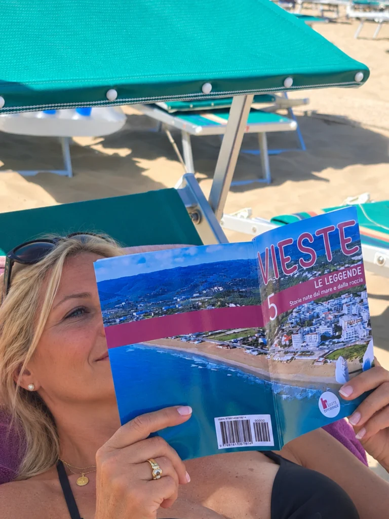 signora in spiaggia che legge la guida n.5 della collana editoriale di Vieste Experience, Le leggende di Vieste.