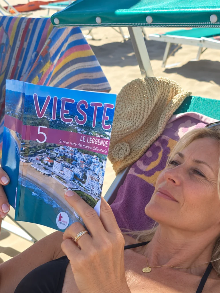 signora in spiaggia che legge la guida n.5 della collana editoriale di Vieste Experience, Le leggende di Vieste.