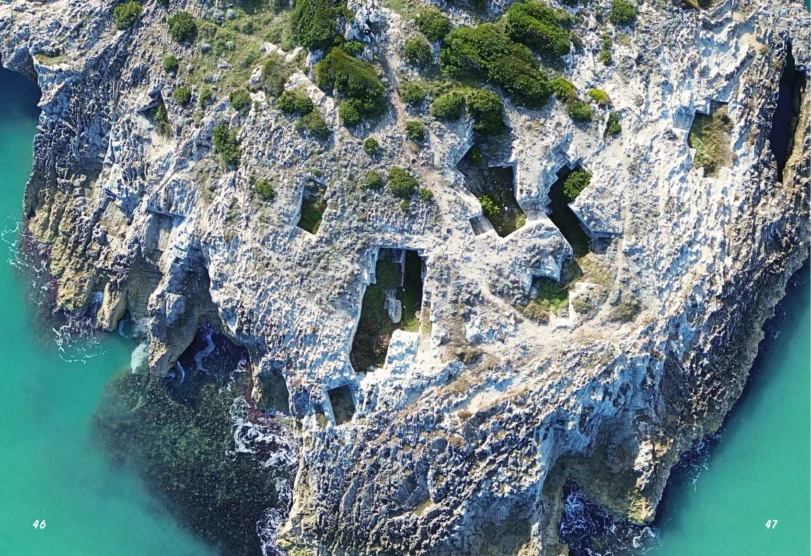 file anteprima pag._Tavola disegno 1 copia 24 Guida n.2 Storia e cultura di Vieste, guida aperta alla doppia pagina caratterizzata da una immagine a tutta grandezza che riprende alcuni scavi di Tufo dall'alto con un drone.